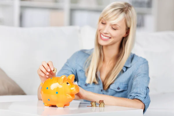 Lachende vrouw dropping munten in piggy bank — Stockfoto