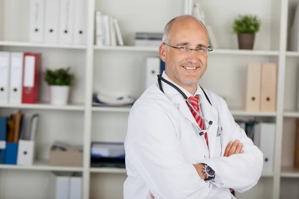 Male Doctor With Arms Crossed Standing Against Shelves — Stock Photo, Image