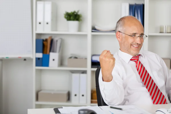 Geschäftsmann mit geballter Faust feiert Sieg am Schreibtisch — Stockfoto