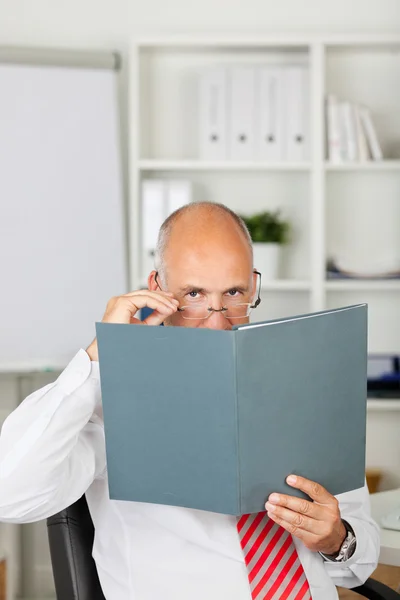 Empresário espreitando o arquivo no escritório — Fotografia de Stock