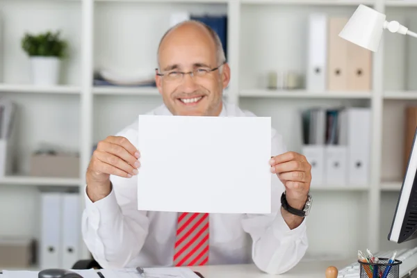 Gelukkig zakenman houden blanco papier op Bureau — Stockfoto