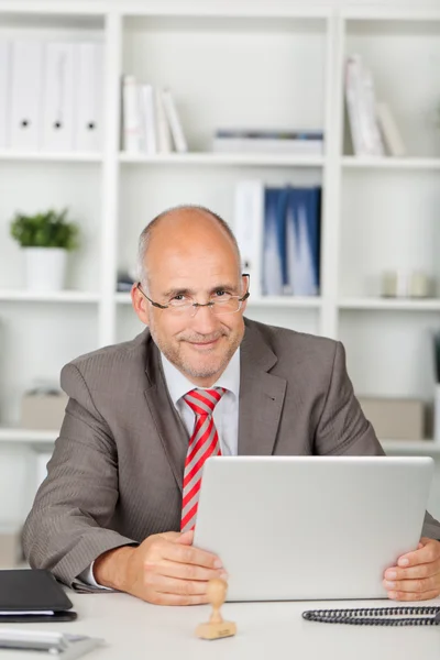 Приветливый бизнесмен сидит за столом с ноутбуком — стоковое фото