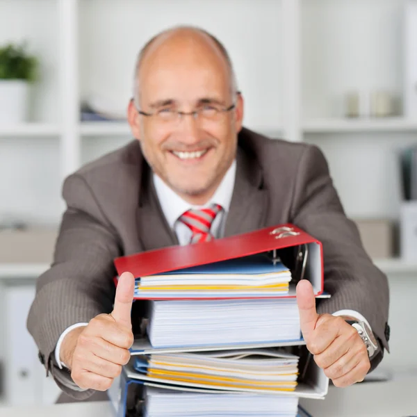 Empresario con pila de libros gestos pulgares hacia arriba — Foto de Stock