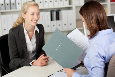 Businesswoman Reading Female Candidate's CV At Desk clipart