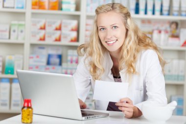Pharmacist Holding Prescription Paper While Using Laptop At Coun clipart