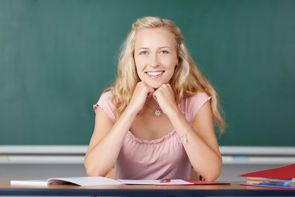 Kvinnlig lärare med händerna på hakan sitter vid skrivbord — Stockfoto