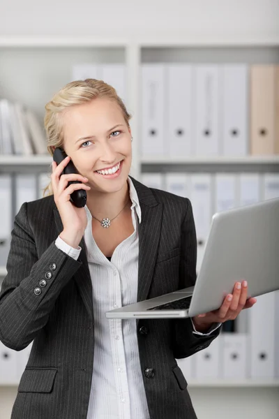 Mujer de negocios con el ordenador portátil usando el teléfono móvil en la oficina — Foto de Stock