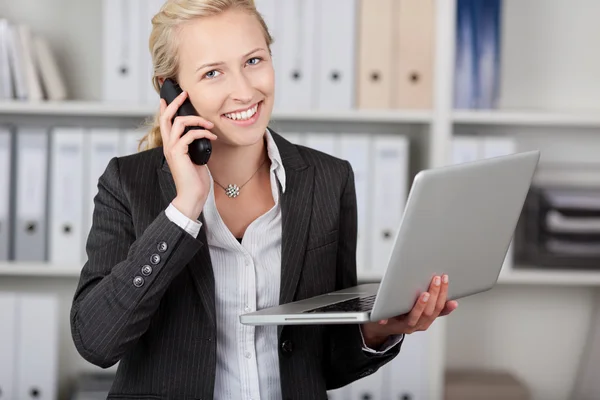 Femme d'affaires avec ordinateur portable utilisant le téléphone dans le bureau — Photo