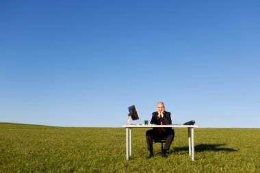 Businessman Sitting At Desk On Field Against Sky clipart