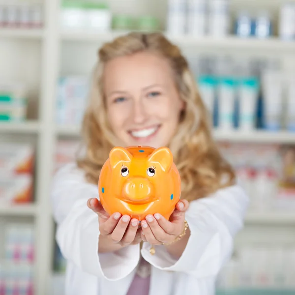 Fiatal női gyógyszerész gazdaság Piggybank — Stock Fotó