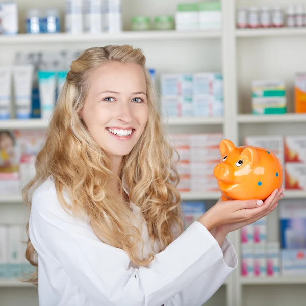 Young Female Pharmacist Smiling With Piggy Bank — Stock Photo, Image