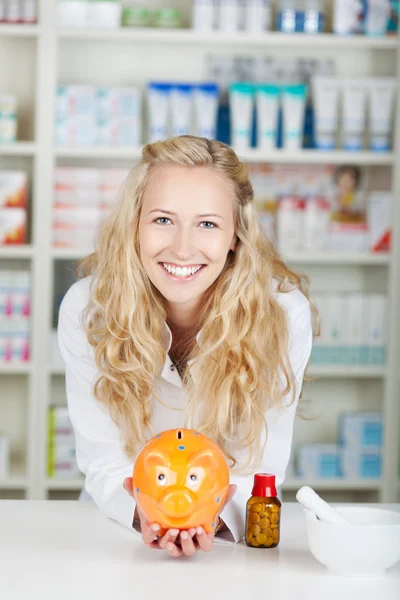 Junge Apothekerin mit Sparschwein — Stockfoto