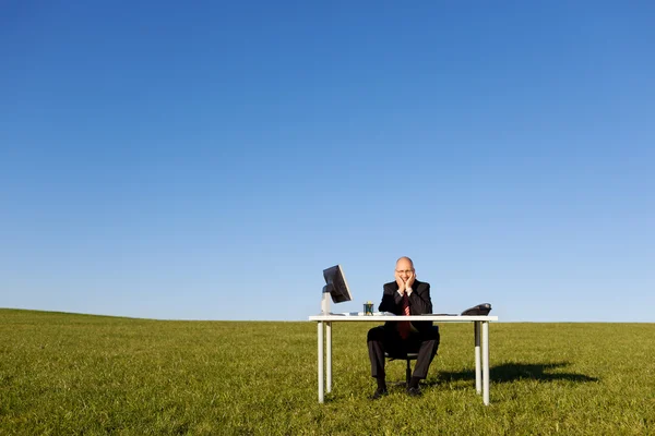 Affärsman som sitter vid skrivbord på fältet mot himlen — Stockfoto