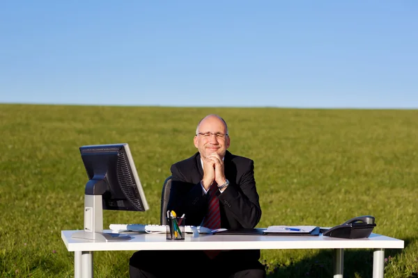 Zakenman met handen geklemd zit aan Bureau op veld — Stockfoto