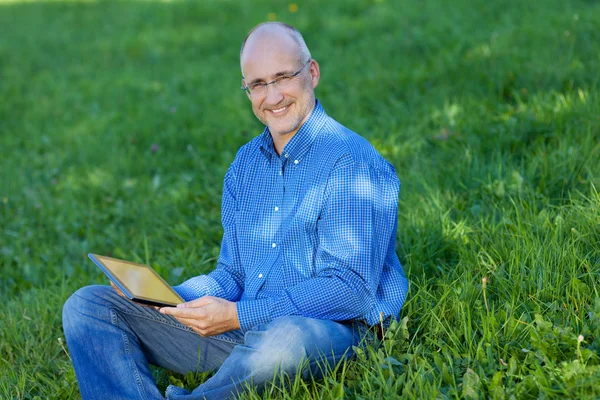 Homme d'affaires tenant tablette numérique tout en étant assis sur l'herbe — Photo