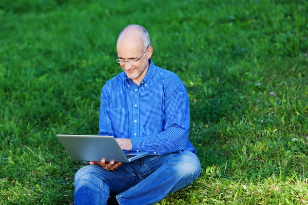 Homme d'affaires en utilisant un ordinateur portable tout en étant assis sur l'herbe — Photo