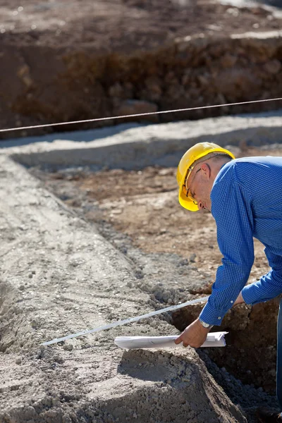 Arquitecto sosteniendo el plano mientras usa cinta métrica en Constr —  Fotos de Stock