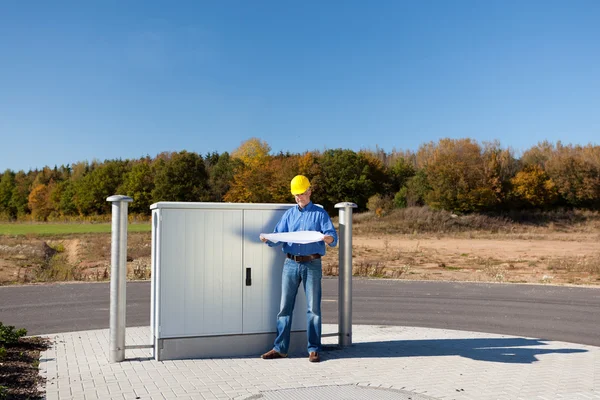 Architect bedrijf blauwdruk terwijl staande tegen elektrische vak — Stockfoto