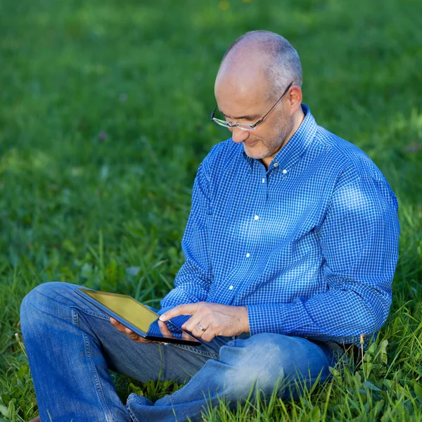 Człowiek posiadający cyfrowy tablicowy siedząc na trawie — Zdjęcie stockowe