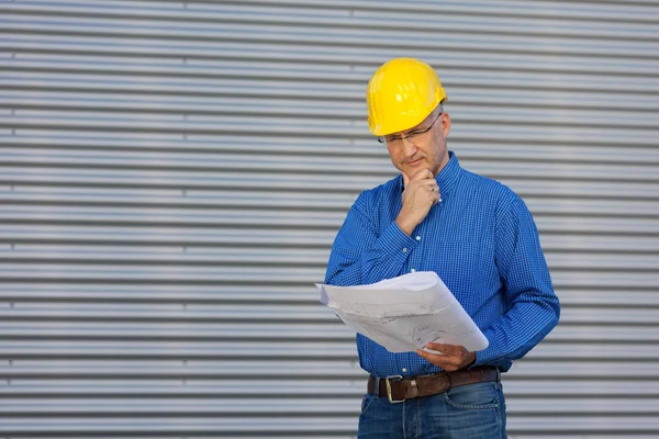 Architect With Hand On Chin Looking At Blueprint Against Shutter — Stock Photo, Image