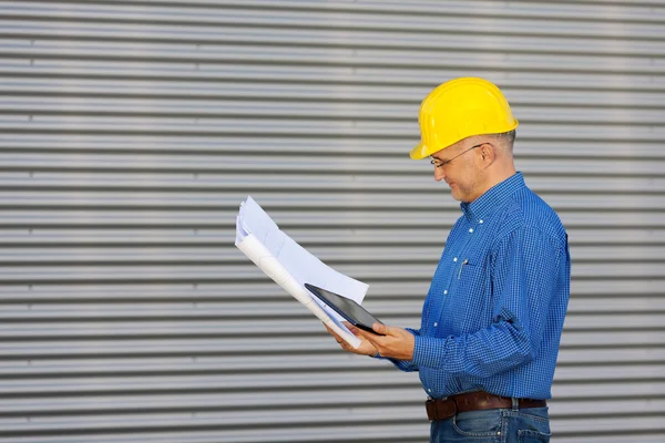 Architekt hält digitales Tablet in der Hand, während er den Bauplan betrachtet — Stockfoto