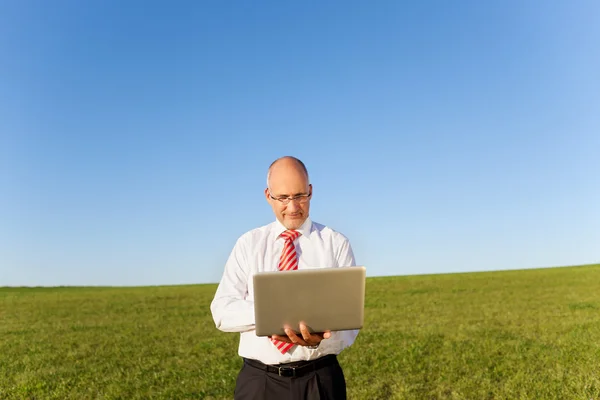 Empresário segurando laptop no campo gramado — Fotografia de Stock
