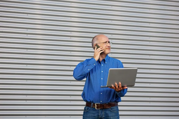 Zakenman met laptop met behulp van mobiele telefoon terwijl u weg — Stockfoto