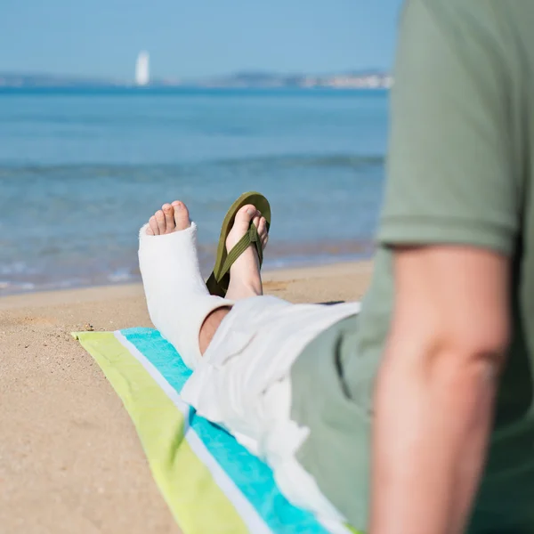 Man med gips avkopplande på stranden — Stockfoto