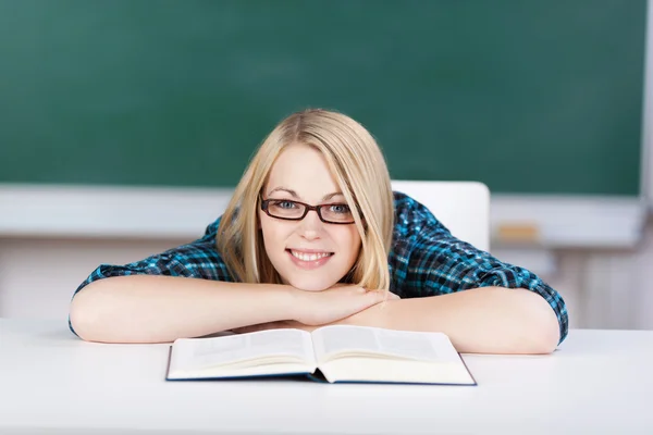 Vrouwelijke student met boek leunend op Bureau in klas — Stockfoto