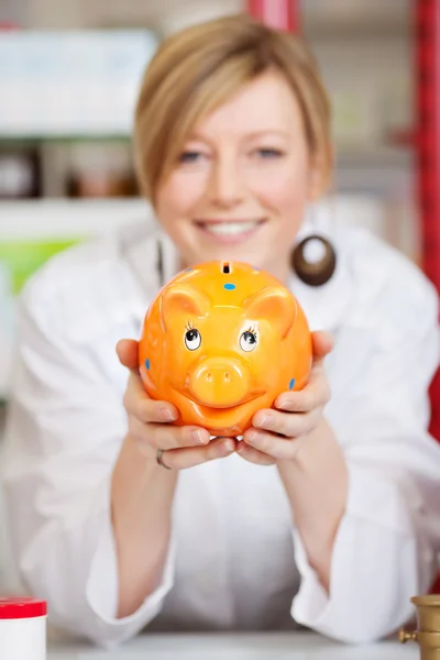 Pharmacist with piggy bank in the pharmacy — Stock Photo, Image