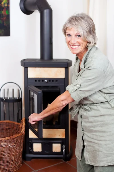 Senior lady puting wood in the stove — Stock Photo, Image