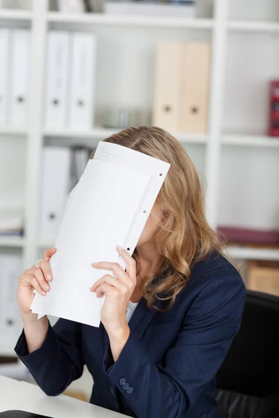 Zakenvrouw die betrekking hebben op gezicht met documenten in Bureau — Stockfoto