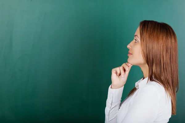 Enseignant réfléchi avec la main sur le menton contre le tableau — Photo