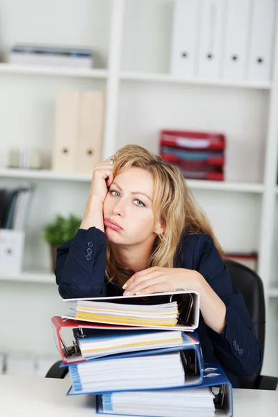 Gelangweilte Geschäftsfrau lehnt an gestapelten Ordnern am Schreibtisch — Stockfoto