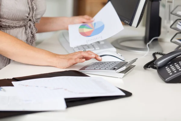 Zakenvrouw piechart houden tijdens het gebruik van Rekenmachine op Bureau — Stockfoto