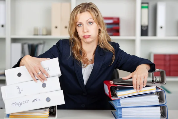 Gelangweilte Geschäftsfrau hinter gestapelten Aktenordnern am Schreibtisch — Stockfoto