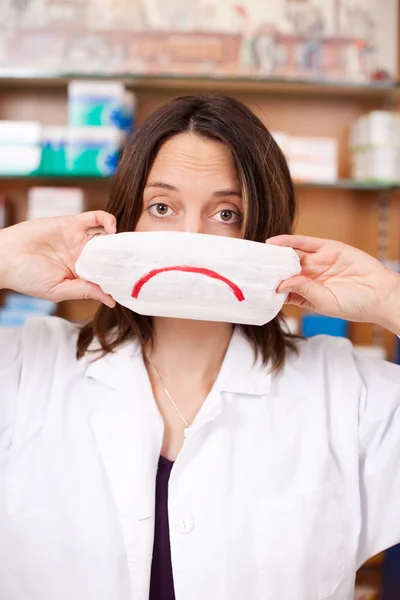 Feminino farmacêutico segurando máscara com Sad Smiley — Fotografia de Stock