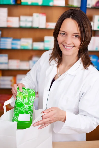 Apothekerin legt Medikamentenpackung in Tüte an die Theke — Stockfoto