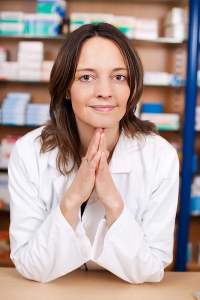 Kvinnliga farmaceut med händerna knäppta på apotek counter — Stockfoto