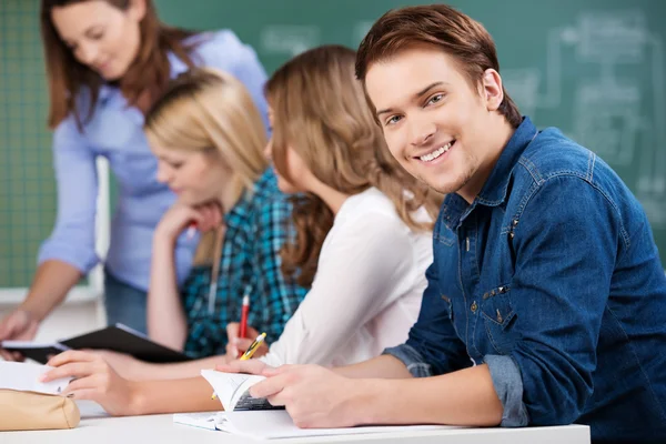 Male Student Holding Book With Classmates And Teacher At Desk Royalty Free Stock Photos