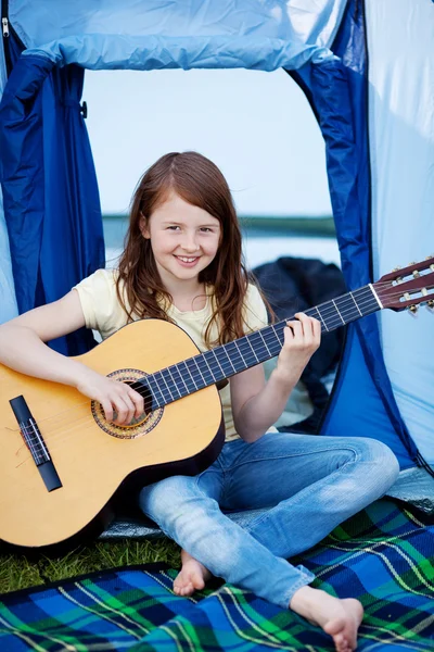 Chica joven tocando la guitarra contra la tienda — Foto de Stock