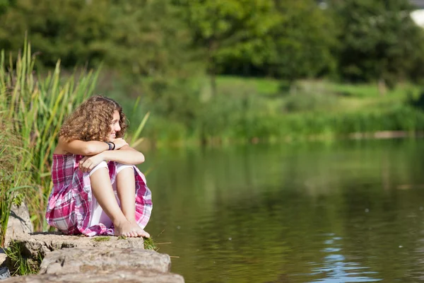 Ragazza adolescente seduta sulla roccia guardando lontano dal lago — Foto Stock