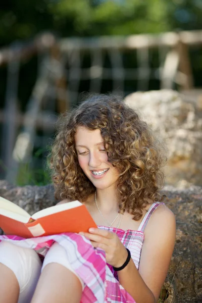 Дівчина читає книгу спираючись на рок — стокове фото