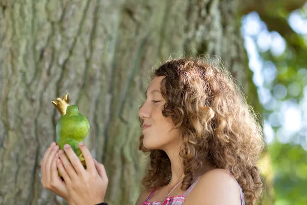 Adolescente chica besos juguete rana contra árbol tronco — Foto de Stock