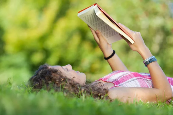 Menina leitura livro enquanto deitado na grama — Fotografia de Stock