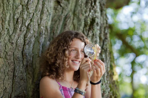 Девушка смотрит на лист через увеличительное стекло в парке — стоковое фото