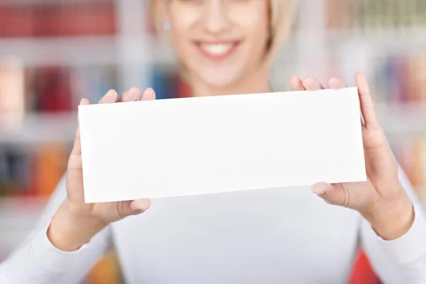 Joven mujer sosteniendo el signo en blanco en la biblioteca — Foto de Stock