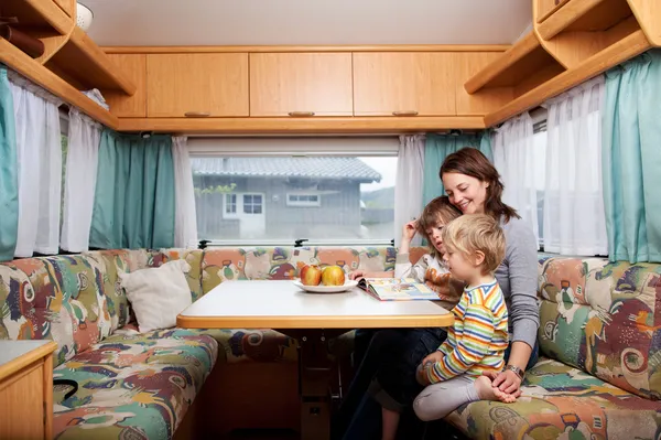 Mujer con hijos leyendo libro de cuentos en la mesa en caravana — Foto de Stock