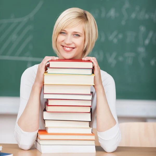 Lachende vrouw in klaslokaal op gestapelde boeken — Stockfoto