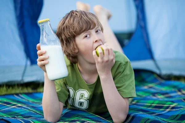 Chłopiec trzyma butelkę mleka i jedzenia jabłko leżąc na koc — Zdjęcie stockowe
